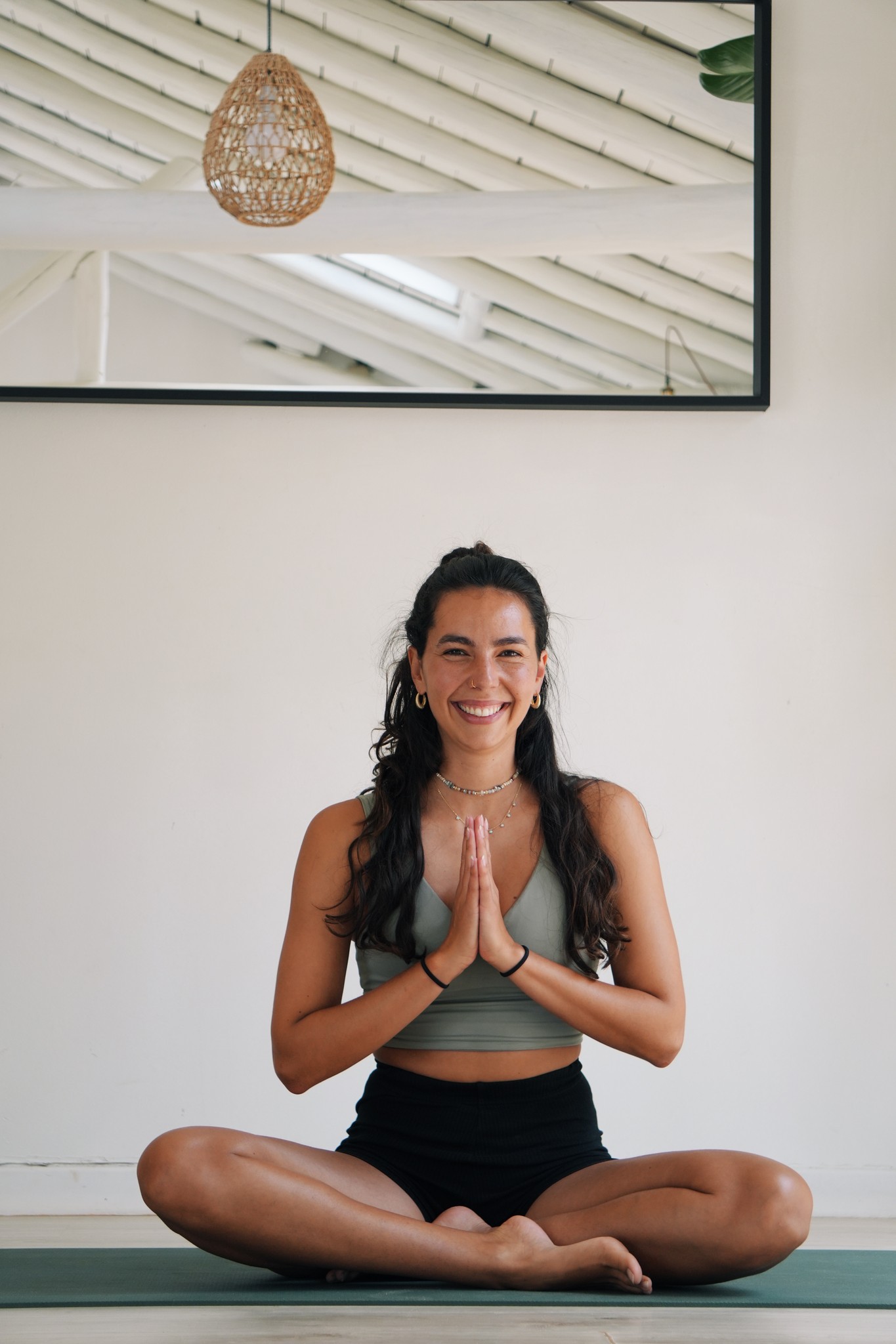 Alanis sitzt im Schneidersitz auf der Yogamatte, die Hände vor dem Herzen.