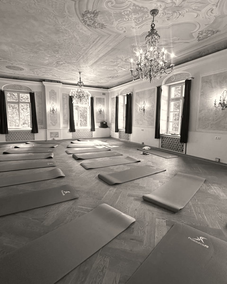 Saal mit Stuckdecke und Kronleuchter, ausgelegte Yogamatten vor Firmenkurs.
